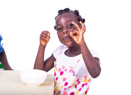 cute little girl sitting at a table facing a cup of coffee, and making a correct gesture.の写真素材