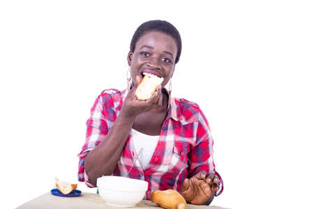 beautiful young woman sitting at the table having breakfast while eating a piece of bread.の写真素材