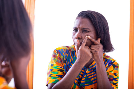 a mature woman standing on white background hugging acne on her face in front of the mirror
