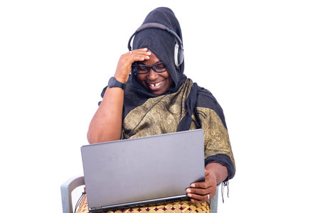 beautiful muslim businesswoman sitting on white background laughing using laptop and headphones.の写真素材