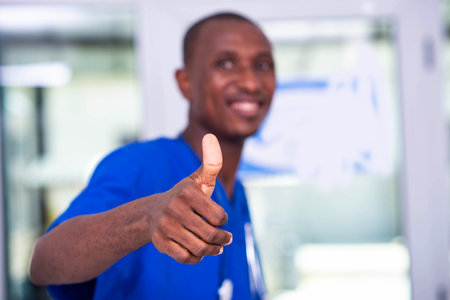 handsome young man doctor in blue uniform with stethoscope, showing screen his thumb while smiling.