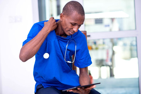 young serious male doctor in blue uniform and stethoscope working on digital tablet.