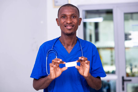 young male doctor in blue uniform with stethoscope, holding a small white box of medication while...