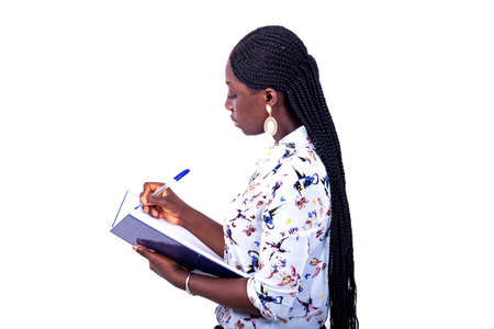 portrait of a beautiful serious young woman standing aside, writing in the notebook with a pen.の写真素材