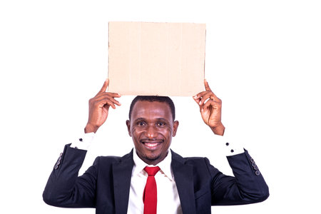 a businessman standing on white background carrying an empty paper on his head and looking at the camera smiling.の写真素材