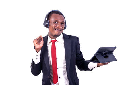 a businessman in jacket standing on white background listening to music using tablet and headphones smiling.の写真素材