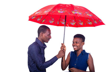 portrait of a young man and woman standing under an umbrella while smiling.の写真素材