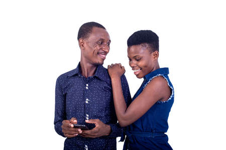 a young couple standing on white background holding cellphone smiling.の写真素材