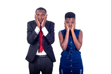 young couple standing on white background with hands on cheeks looking at camera with frightened look.の写真素材