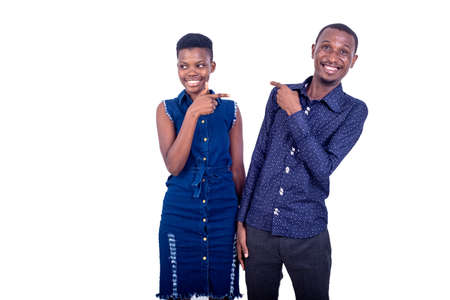 portrait of a young man and woman pointing the index fingers towards each other while smiling at the camera.の写真素材