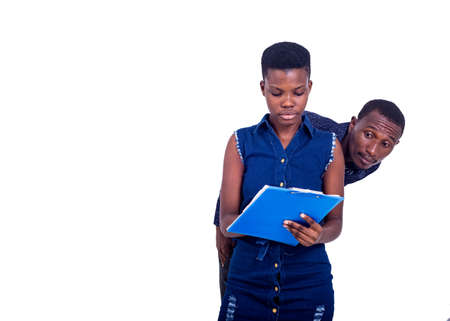 young businessman spies on woman writing to clipboard while hiding behind his back.の写真素材