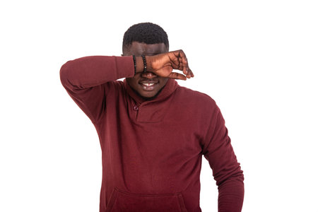 portrait of a handsome young man covering eyes with arm while smiling at the camera.