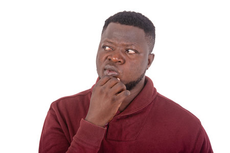 portrait of a handsome young man thinking while holding hand on chin and looking aside.