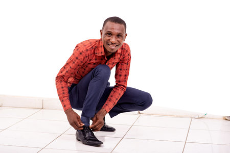 a handsome businessman in a checkered shirt crouching on a white background adjusting his laces, smiling.の写真素材