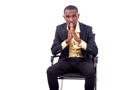 portrait of a handsome serious young businessman sitting on a chair and holding his hands together.の写真素材