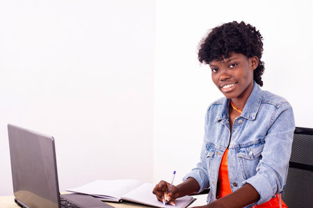 portrait of a young woman taking notes using laptop computer smiling.