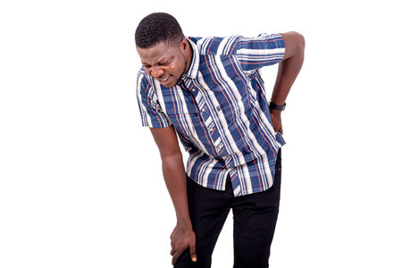 portrait of a handsome young man suffering from back pain, touches back with hand.