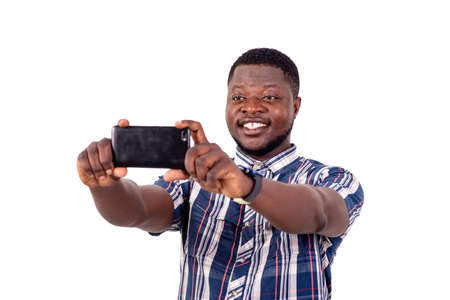 a young man in a short sleeved shirt standing on a white background taking a picture of himself using a mobile phone, smiling.の写真素材