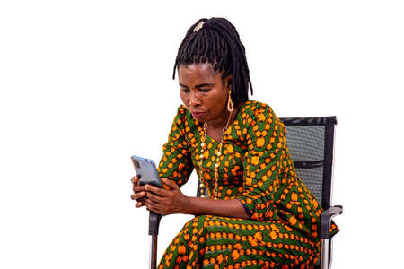 a beautiful mature woman in traditional dress sitting in a chair reading message on cell phone.の写真素材