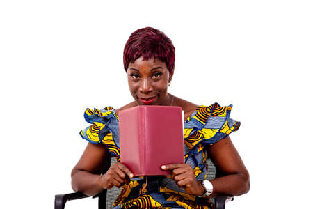 portrait of a beautiful adult business woman sitting on a chair and looking over an open book while smiling.の写真素材