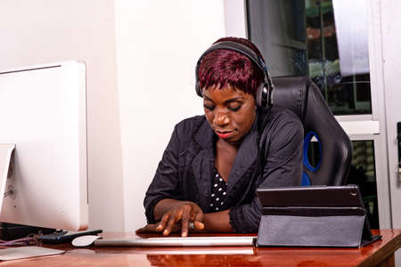 portrait of a beautiful adult business woman sitting at the desk listening to music and working with laptop computer smiling.の写真素材