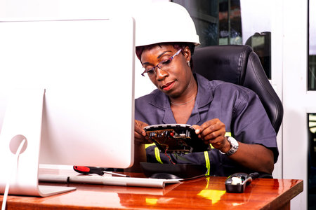 portrait of a beautiful female technician wearing work uniform and white safety helmet repairing a mobile phone with screwdriver.の写真素材