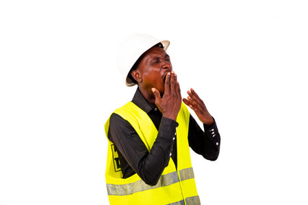 Young tired engineer man wearing green vest and white safety helmet while yawning with hand over...