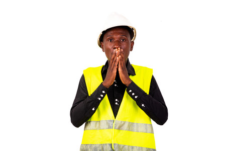 Shocked young engineer man wearing green vest and white safety helmet while covering hands over...