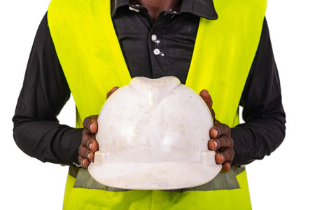 hands of a construction engineer wearing green vest and showing a white hard hat.