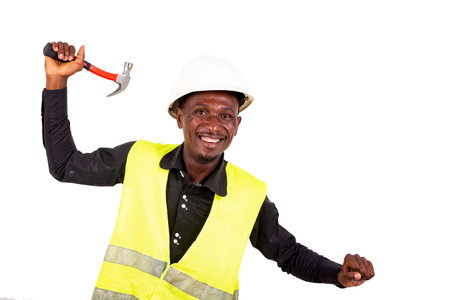 young male technician wearing green vest and safety helmet and holding hammer while smiling.