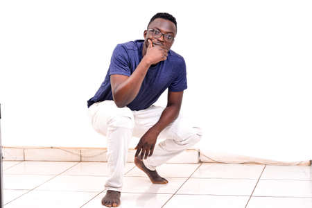 a handsome man in glasses crouching on a white background with bare feet looking at the camera.の写真素材