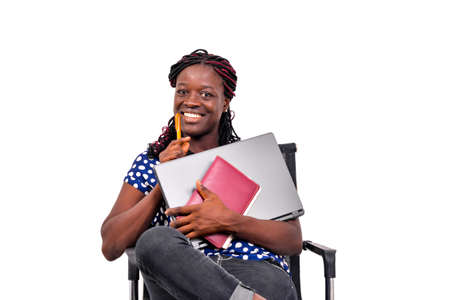 portrait of a beautiful young student girl sitting on a chair and holding a laptop and notebook while smiling.の写真素材