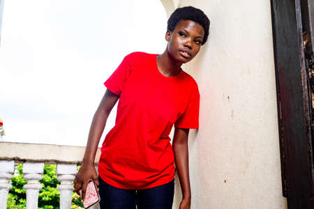 beautiful young girl wearing red t-shirt standing on the balcony of the house with with a spy expression.の写真素材