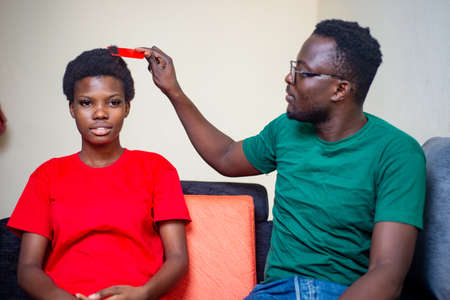 young african couple sitting together in sofa at home, man combing hair of his girlfriend.の写真素材