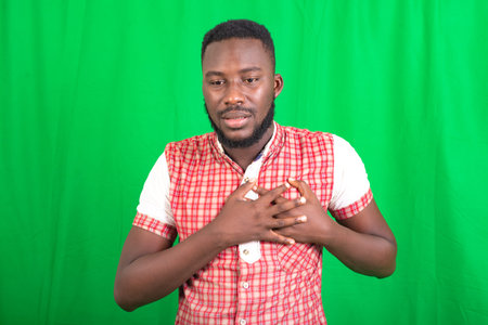 a handsome young bearded man in a shirt standing on background feeling pain in the heart while...
