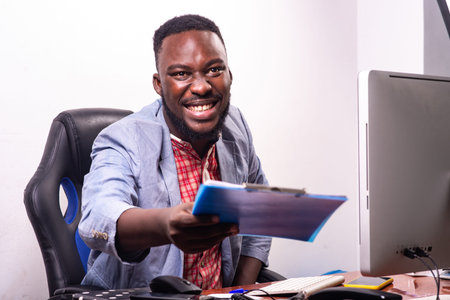 young happy businessman sitting at desk giving clipboard while smiling.