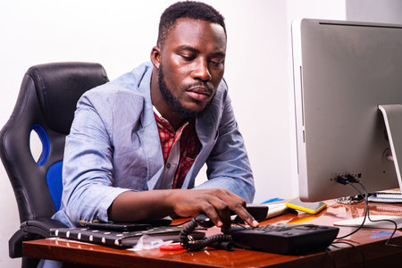 handsome young business man sitting in front of the laptop in the office and dialing number on the...