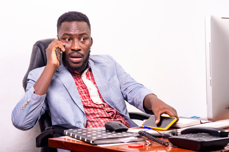 businessman in jacket sitting at desk talking on cellphone.