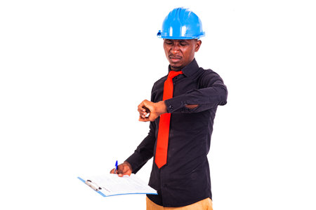 young man engineer wearing blue safety helmet holding clipboard and looking at the time on the wrist watch.の写真素材