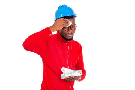 young male construction engineer wearing a blue hard hat and wiping the sweat from his forehead with a white handkerchief.の写真素材