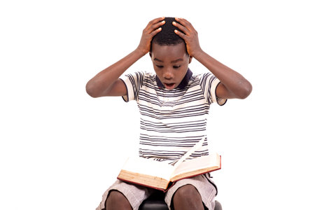 young boy in t-shirt sitting on a beanbag on white background reading a book with surprised.