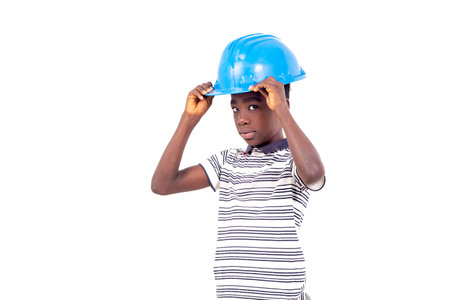 young boy in t-shirt standing on white background adjusting safety hat while looking at camera in profile.の写真素材