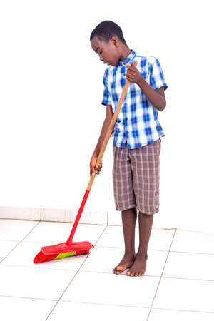 young boy in checkered shirt cleaning room with broom.の写真素材