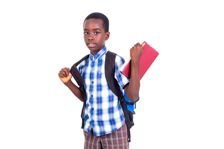 pupil in checkered shirt standing on white background wearing backpack holding book while looking at camera.の写真素材