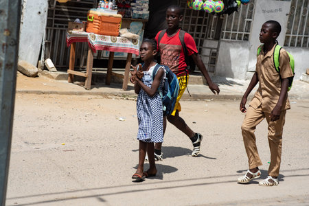 Abidjan, Ivory Coast- March 14, 2022:A young girl and two young boys carrying their bags on their backs, on the road come home from school.のeditorial素材
