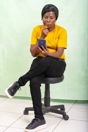 a beautiful mature woman in a yellow t-shirt sitting on a green background looking at cellphone.