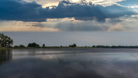 Dramatic sky with sunbeams through the clouds over lake with houses on the shore.の写真素材
