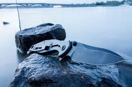 Tactical knife is gray color. Stone. Lake. River. City.の写真素材