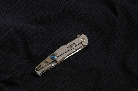 Knife with a metal handle in folded form on black textiles. Iron on black.
