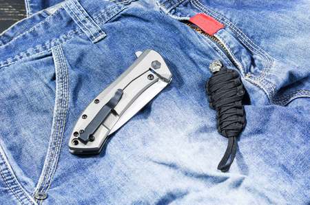 Knife with a metal handle in the folded form. Denim background. Chain of a paracord. Jeans.の写真素材
